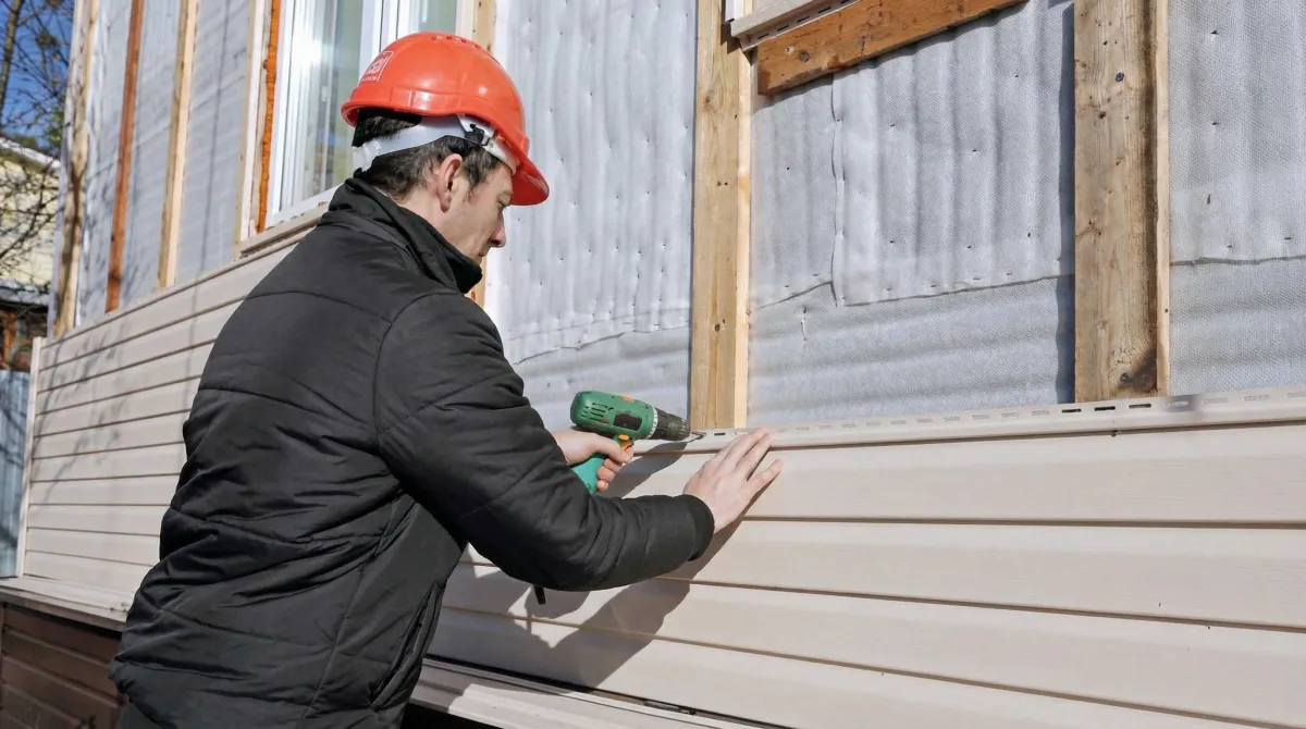 Siding replacement professional using a power drill to install new tan vinyl siding on a home exterior in Chandler, AZ